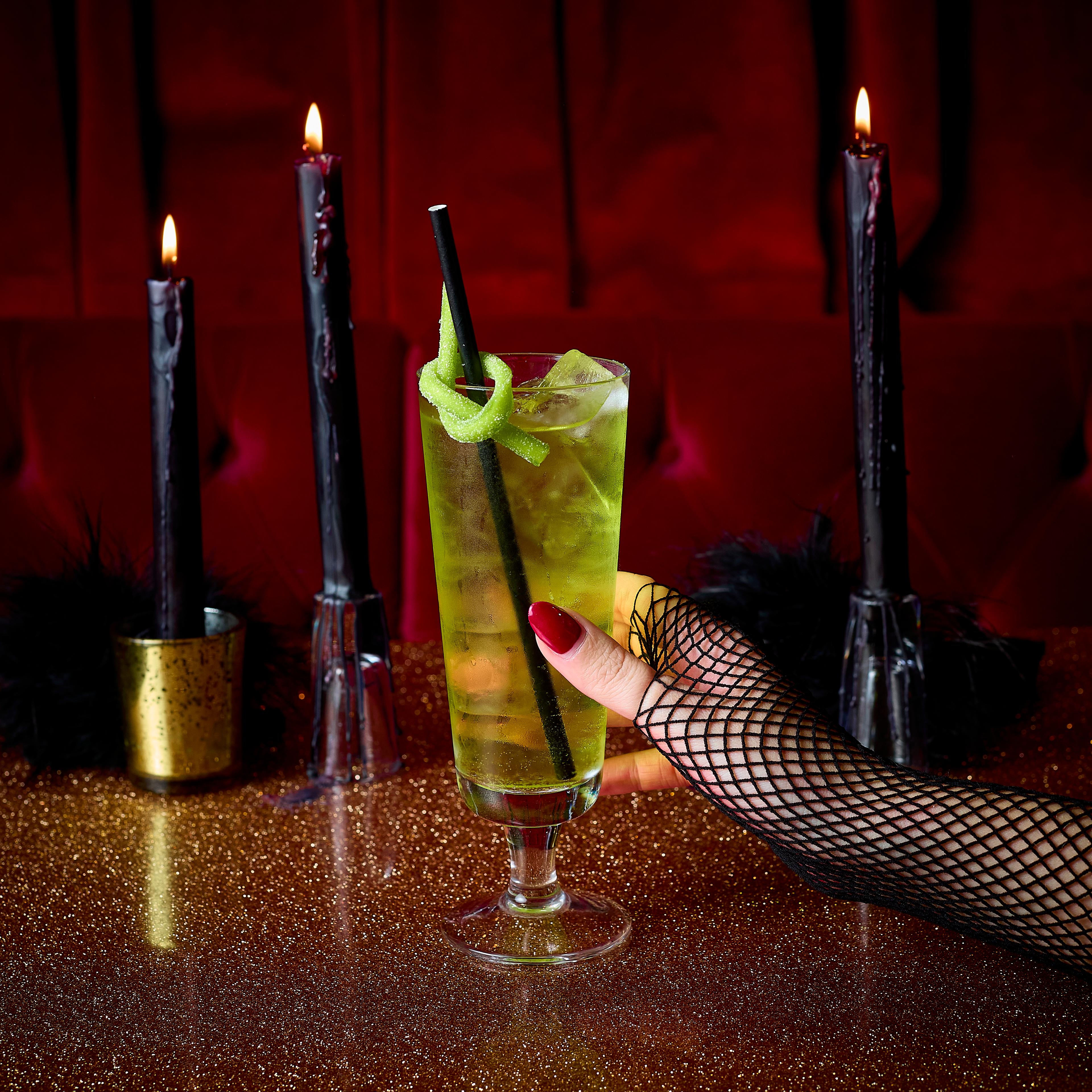 An image of a Halloween green cocktail on a gold table with black candles