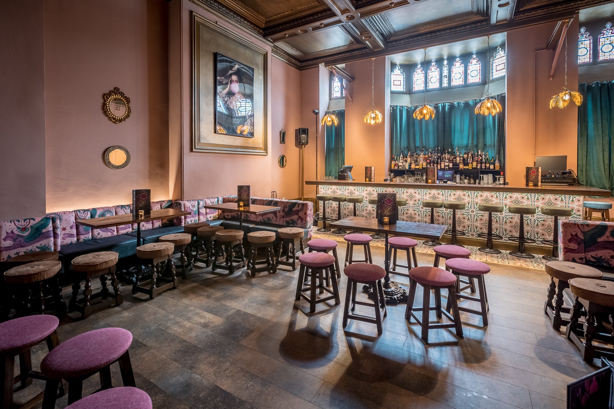 An opulent bar area with pink blush walls and velvet stool seats