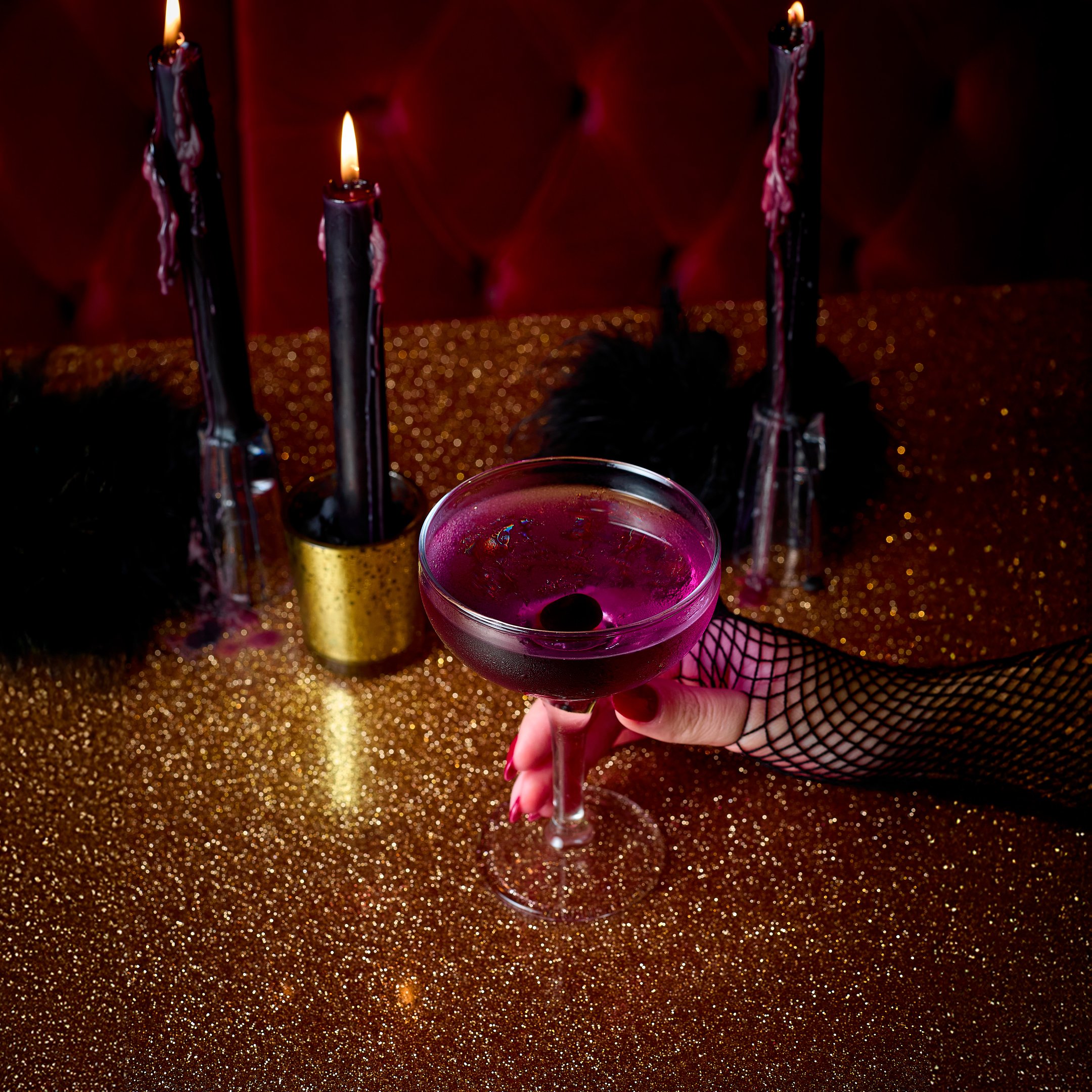 An image of a Halloween purple cocktail on a gold table with black candles