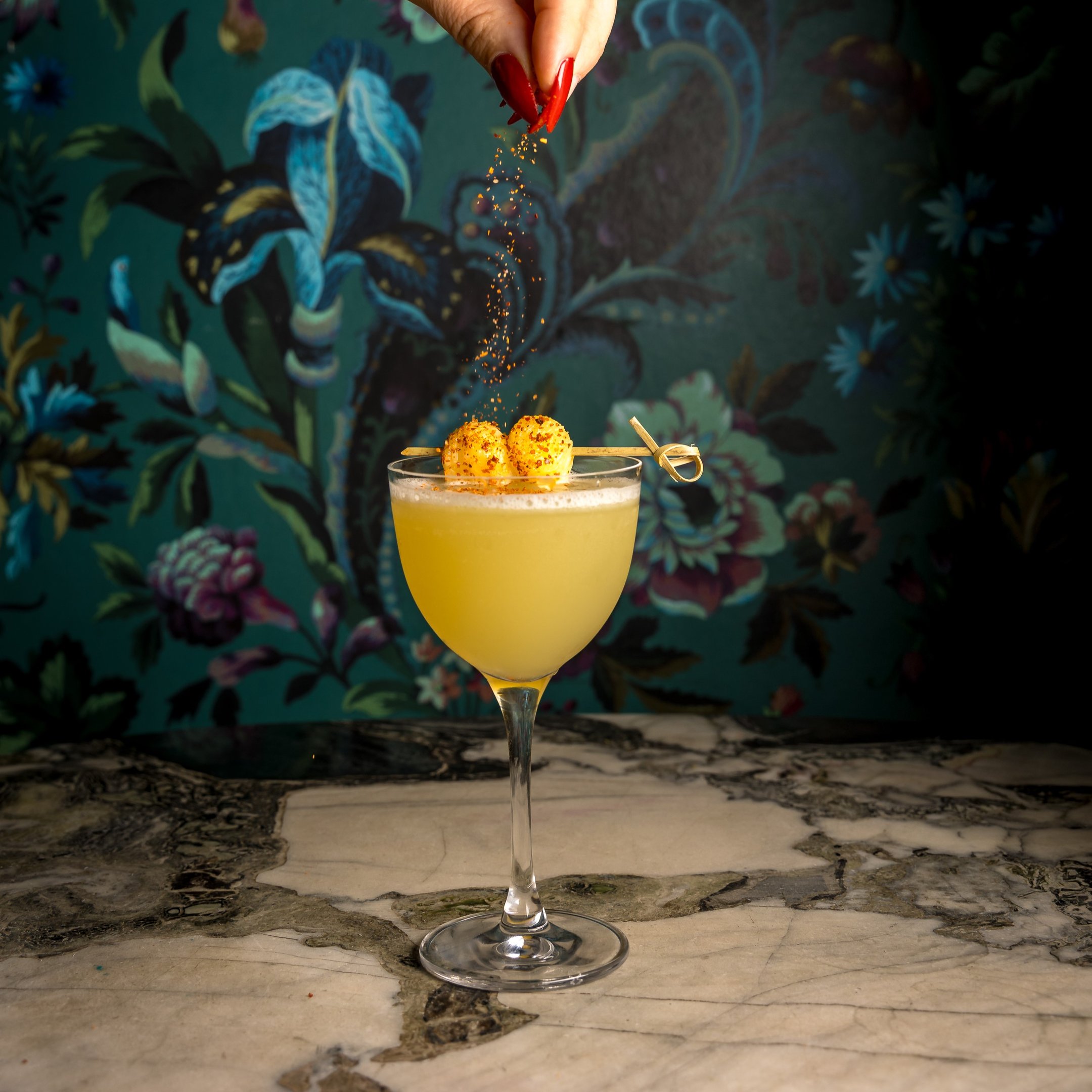 Image of an Alcos Picante cocktail being sprinkled with garnish 