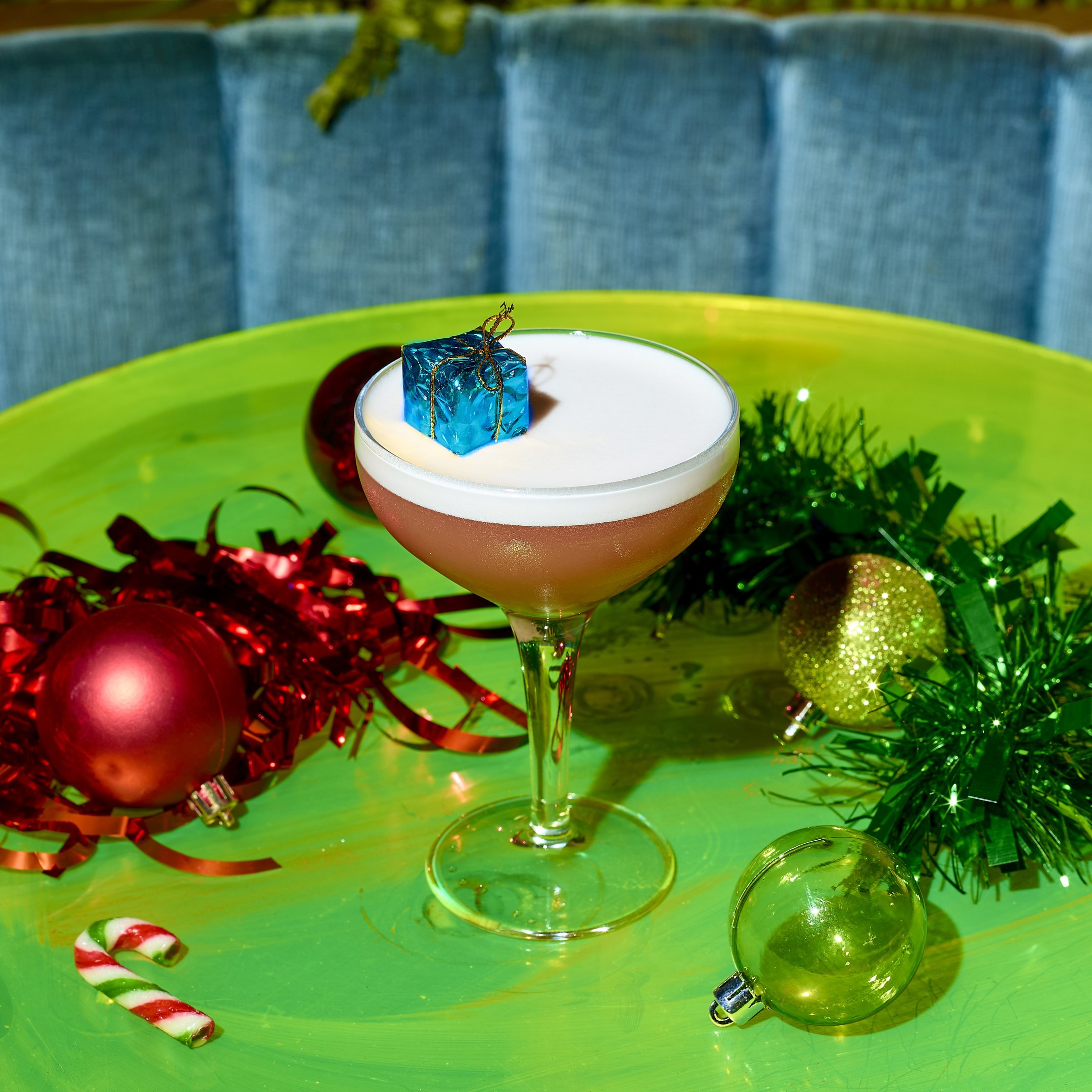 A cocktail in a coupe glass with a mini blue present garnish