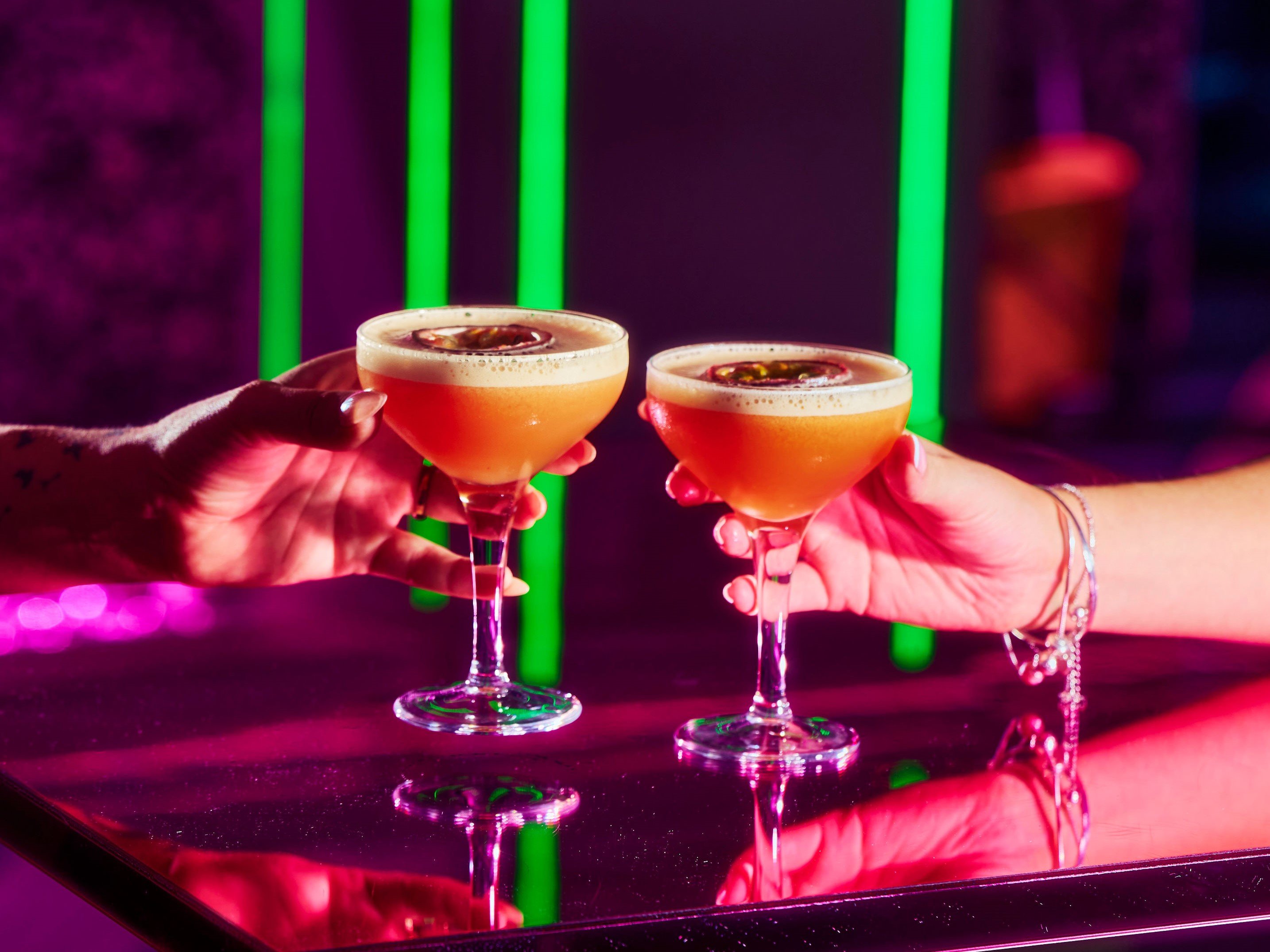 Guests holding pornstar martini cocktails over a table