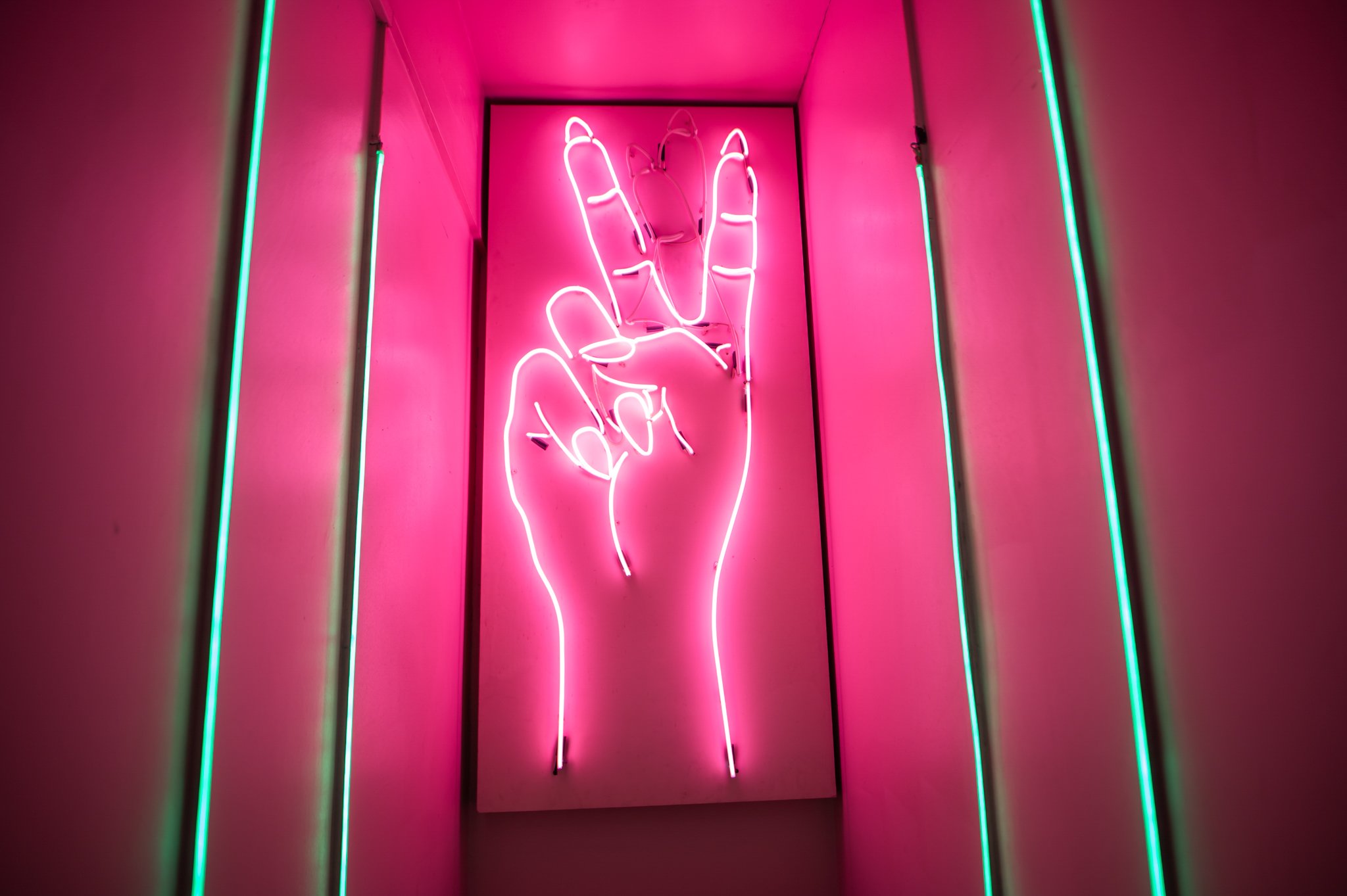 A pink neon sign of a hand doing a peace sign in Tonight Josephine