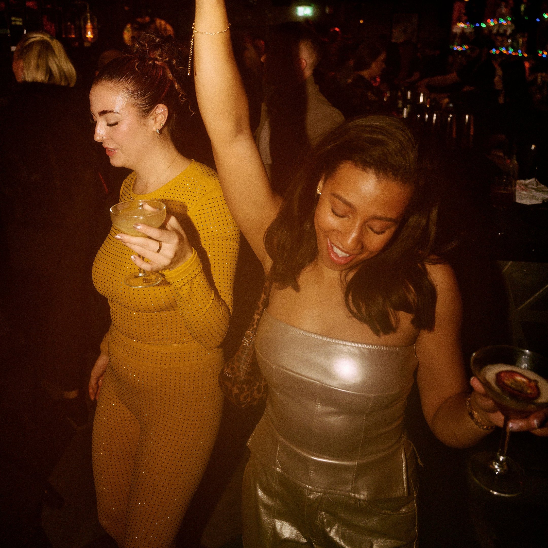 Two women with cocktails in their hands dancing in Dirty Martini