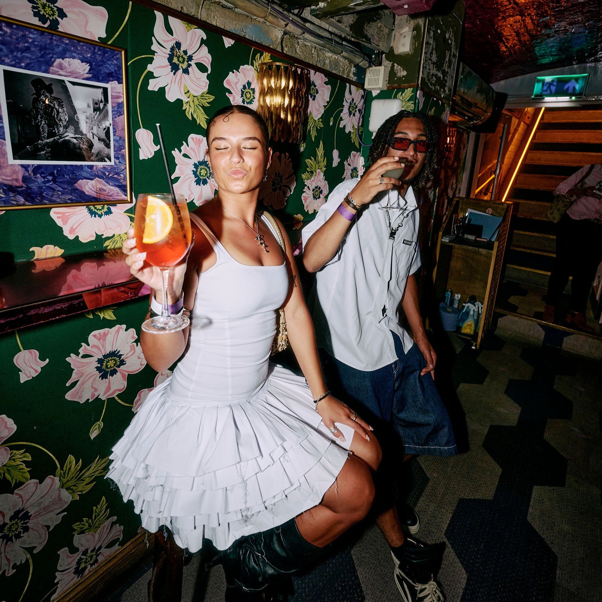 A male and a female guest posing for a photo with drinks in hand in Blame Gloria