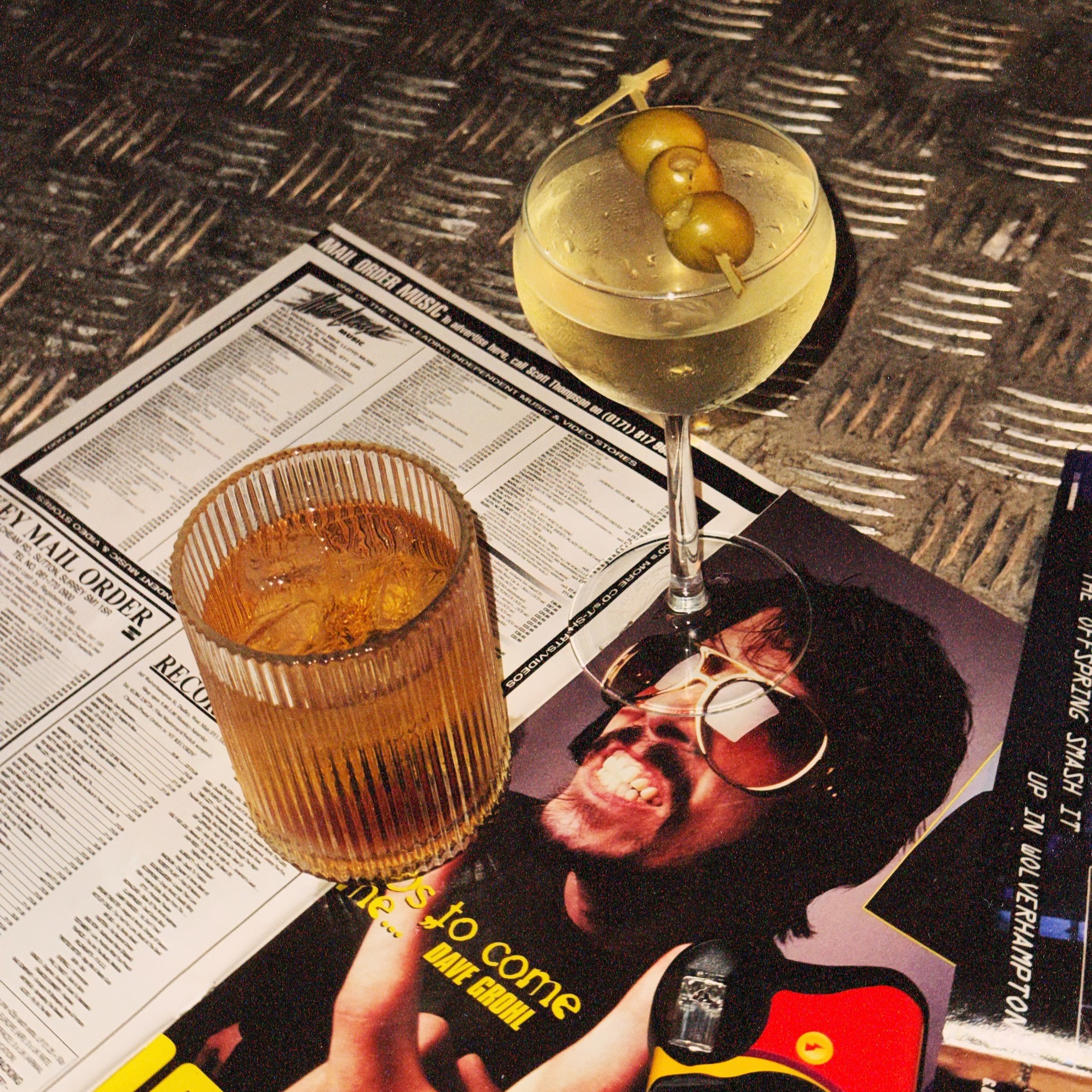 Cocktails sat on top of a magazine next to a disposable camera in Afters