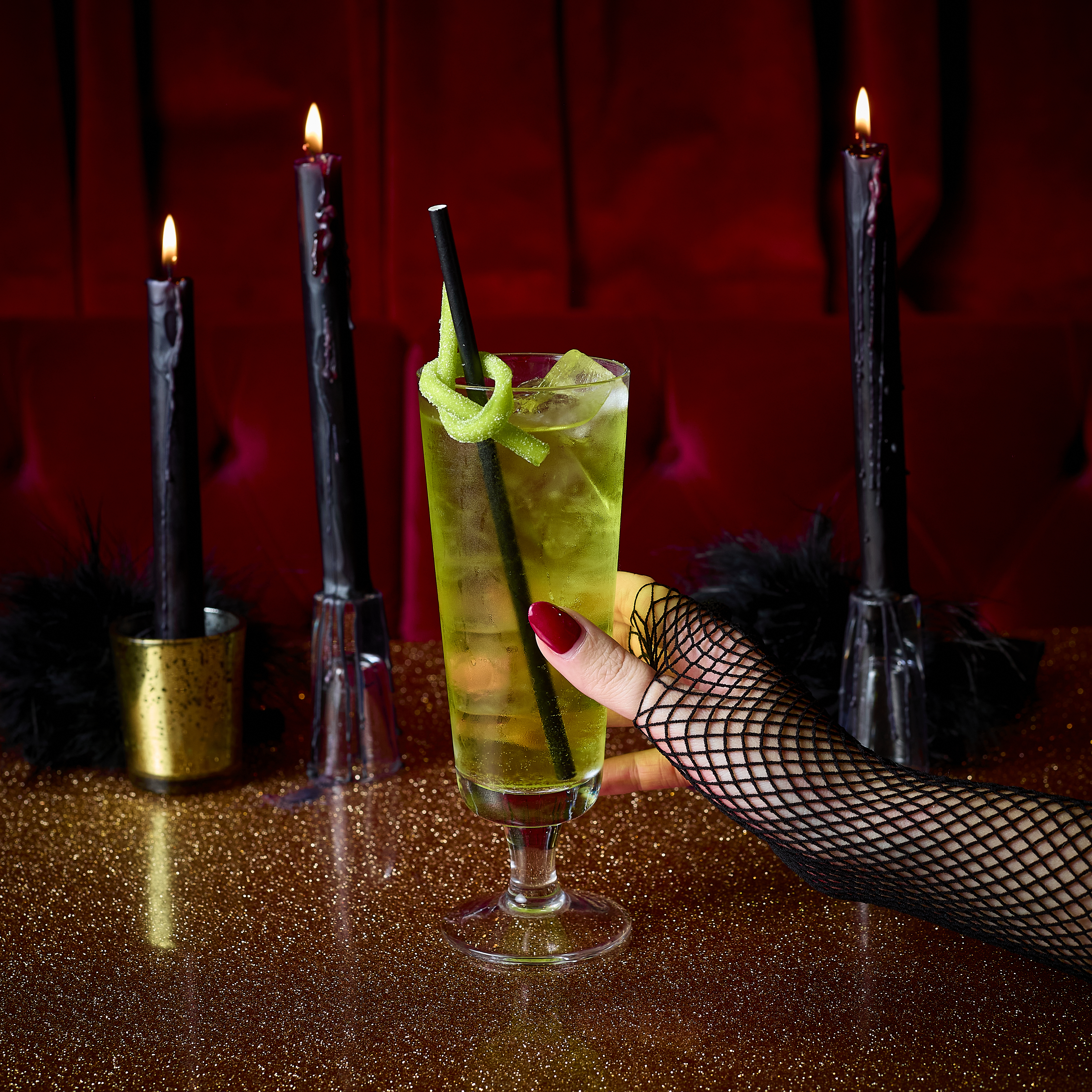 An image of a Halloween green cocktail on a gold table with black candles